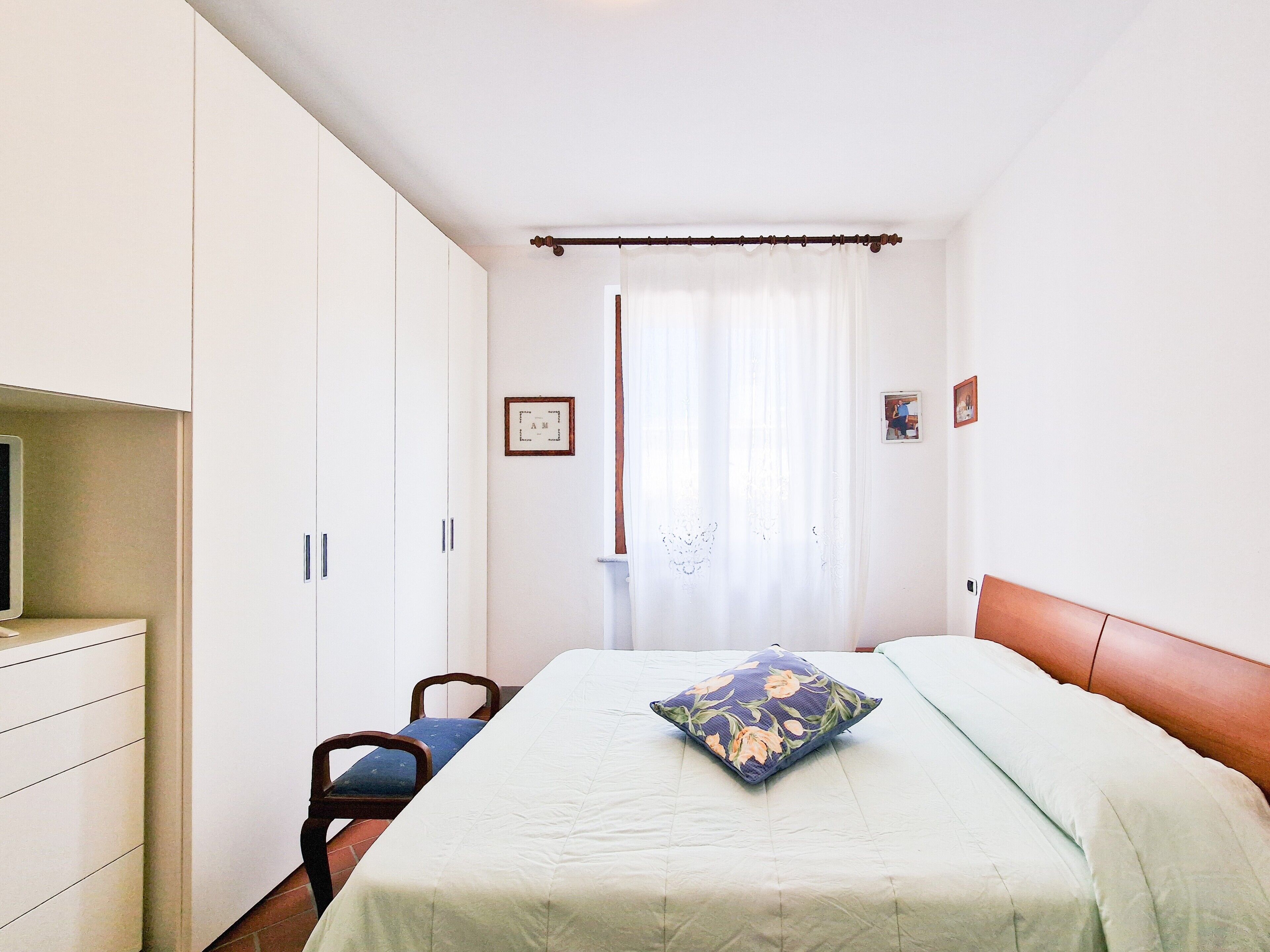 A bedroom with a bed, a chair, a wardrobe, and a window with curtains.