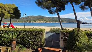 Uma praia com uma estrutura de recreação vermelha, um portão e vista para o mar e colinas.