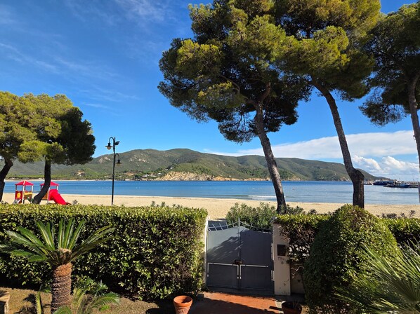 Une plage avec une structure de jeux rouge, une barrière et une vue sur la mer et les collines.