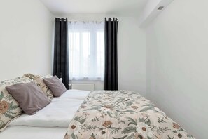 A bedroom with a bed, a window with curtains, and a radiator.