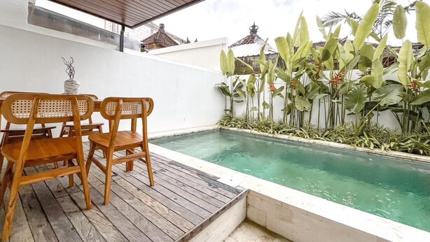 A wooden deck with a pool, surrounded by tropical plants and a white wall. - Villa Morich (Jimbaran)