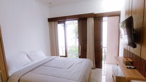 A bedroom with a bed, a TV, a desk, and a window with curtains. - Villa Morich (Jimbaran)