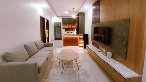A modern living room with a sofa, a coffee table, a TV, and a kitchen in the background. - Villa Morich (Jimbaran)