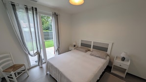 Ein Schlafzimmer mit Bett, Stuhl, Nachttisch und einem Fenster mit Vorhängen.