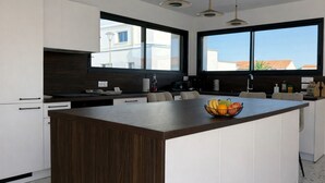 Uma cozinha moderna com uma ilha central, grandes janelas e vista para prédios.