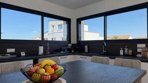 Uma cozinha moderna com uma mesa de jantar, uma fruteira e grandes janelas.