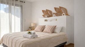 Quarto com cama, almofadas, mesa de cabeceira, luminária e um objeto decorativo na parede.