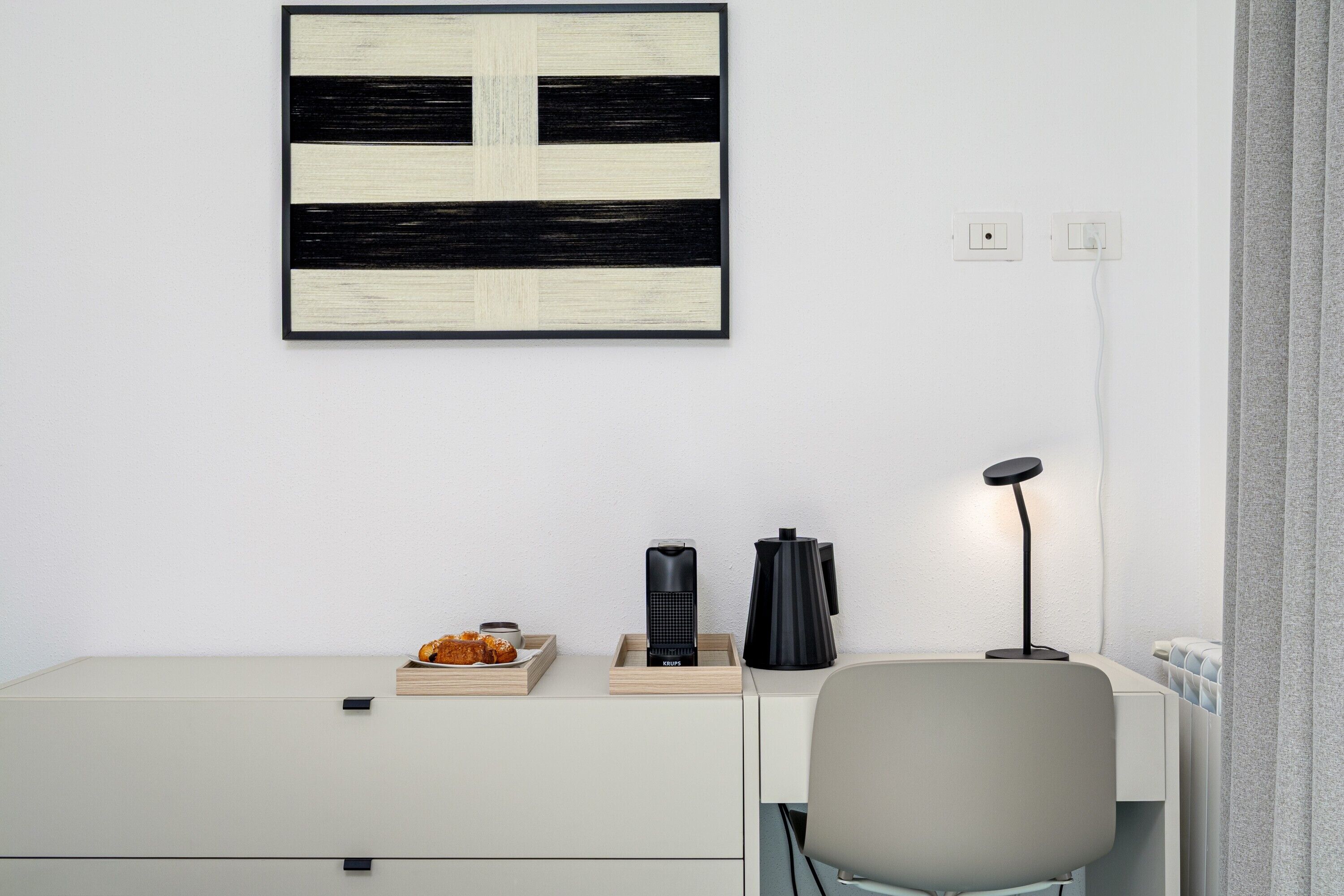 Un bureau minimaliste avec une chaise, une lampe noire et une œuvre d’art abstraite encadrée accrochée au mur.