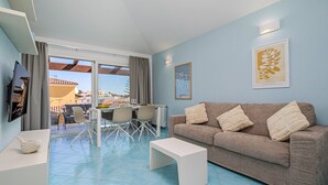 Een woonkamer met een bank, een salontafel, een televisie en een eethoek met stoelen en een tafel.