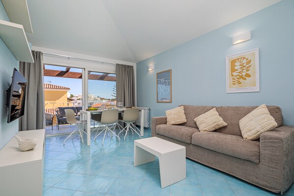 A living room with a sofa, a coffee table, a TV, and a dining area with chairs and a table.