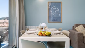 Een eethoek met een tafel voor twee, een schaal fruit en een kunstwerk in een lijst aan de muur.