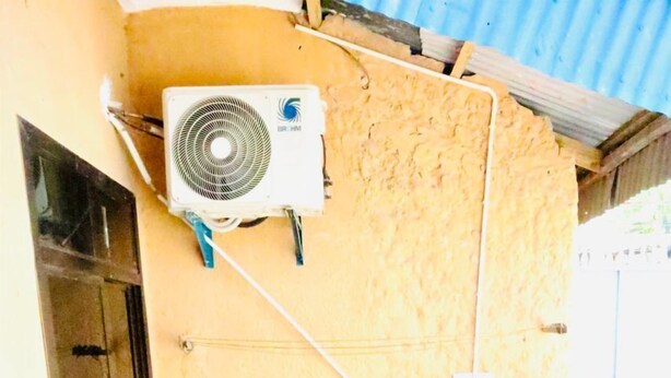 A small outdoor area with a wooden chair, a potted plant, a water dispenser, and an air conditioning unit mounted on the wall. - Mikocheni B-1BR affordable price  (Dar es Salaam)