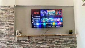 Een flatscreen televisie bevestigd aan een muur met een stenen patroon, een plank eronder en een kleine plant aan de rechterkant.