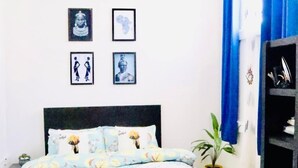 Een slaapkamer met een bed, plafondventilator, aan de muur hangende foto’s en een potplant.