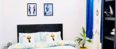 Un dormitorio con cama, ventilador de techo, cuadros en la pared y una planta en maceta.