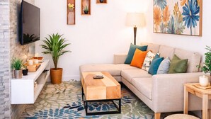 A living room with a sofa, coffee table, TV, and decorative plants. - Mikocheni B-1BR affordable price  (Dar es Salaam)