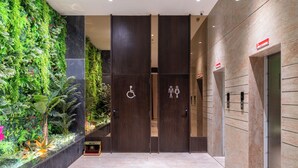 Un hall d’entrée moderne agrémenté d’un jardin vertical, d’un comptoir d’accueil et d’un panneau indiquant l’emplacement des toilettes accessibles aux personnes handicapées.