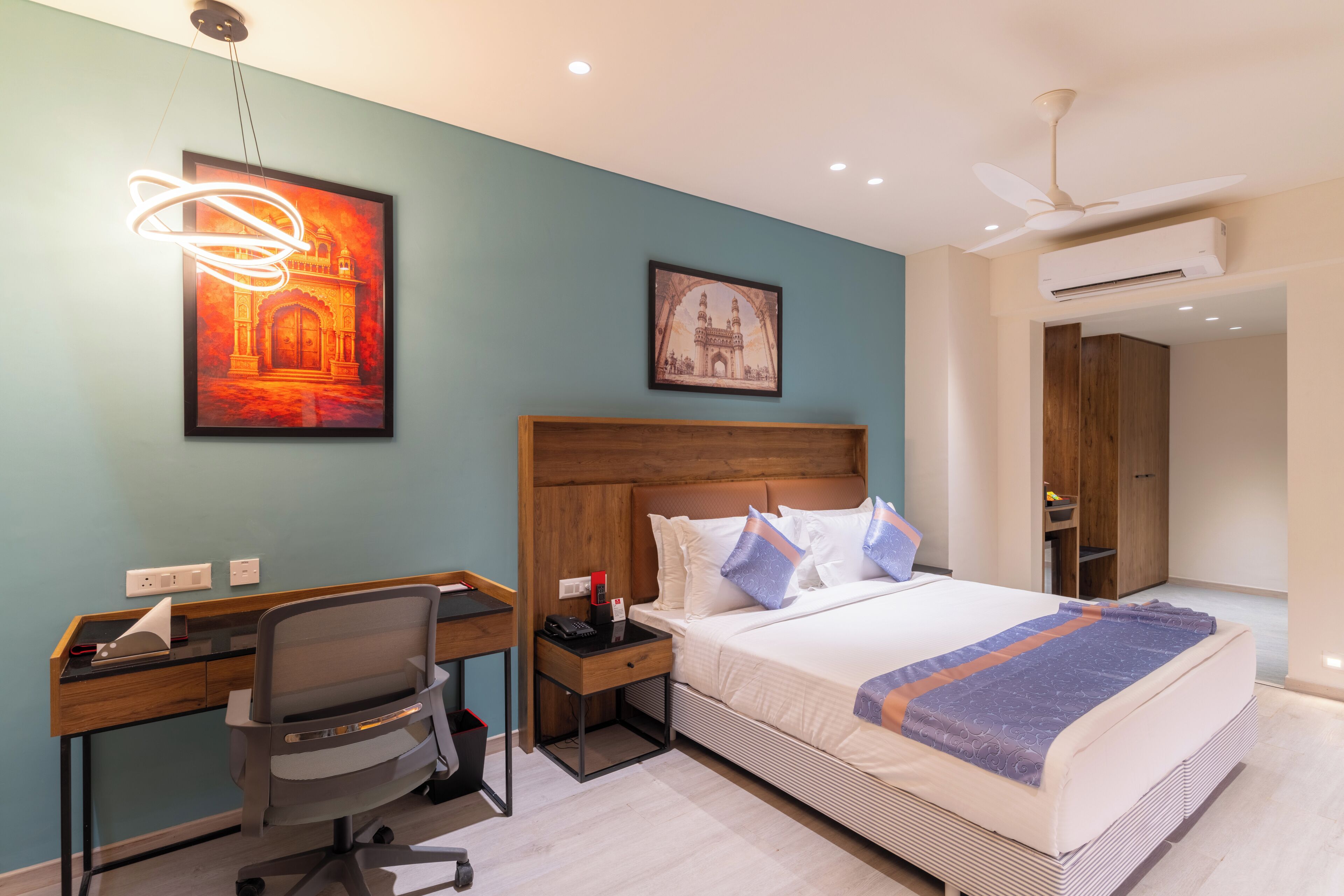 Ein Hotelzimmer mit Bett, Schreibtisch, Stuhl und Bildern an den Wänden.