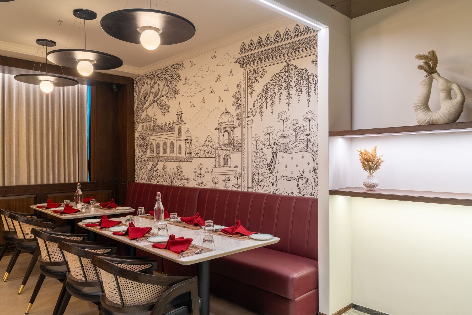 A restaurant with a mural of a traditional building, red upholstered seating, and pendant lighting.