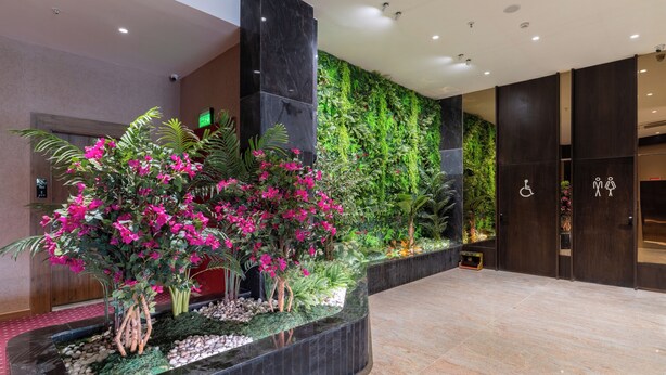 Un hall d’entrée doté d’un sol en marbre, d’un grand bac à fleurs orné de fleurs roses, d’un jardin vertical verdoyant et de panneaux muraux en bois.
