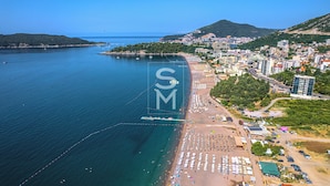 An aerial view of a coastal city with a beach, buildings, and a hilly landscape. - Ststus M apartments 138 (Becici)