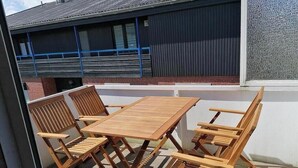 Une table et des chaises en bois sur un balcon donnant sur un immeuble.