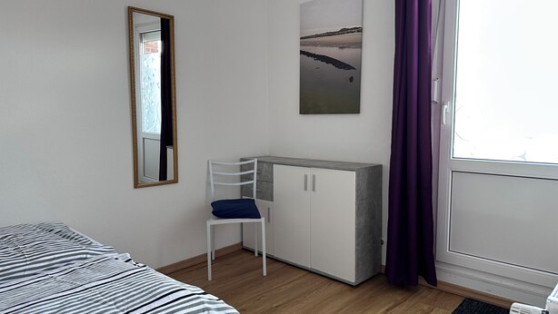 Une pièce comprenant un lit, un bureau avec des placards, une chaise, une fenêtre avec des rideaux et un tableau accroché au mur.
