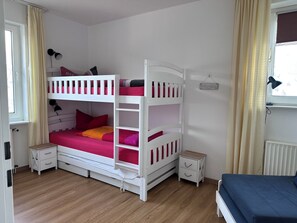 A bunk bed with pink bedding, a bedside table, a nightstand, and a window with curtains.