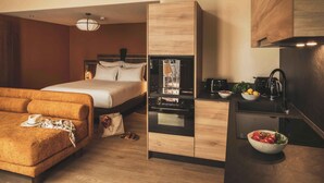 Una habitación de hotel compacta con cama, sofá, kitchenette y televisor integrado.