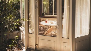Un patio cubierto con una mesa y sillas, rodeado de plantas y una casa al fondo.