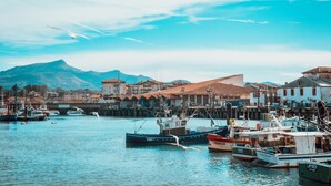 A coastal town with boats docked in the harbor, buildings with red roofs, and a mountain in the background. - Spacieux appt près de la plage avec terrasse (Saint-Jean-de-Luz)
