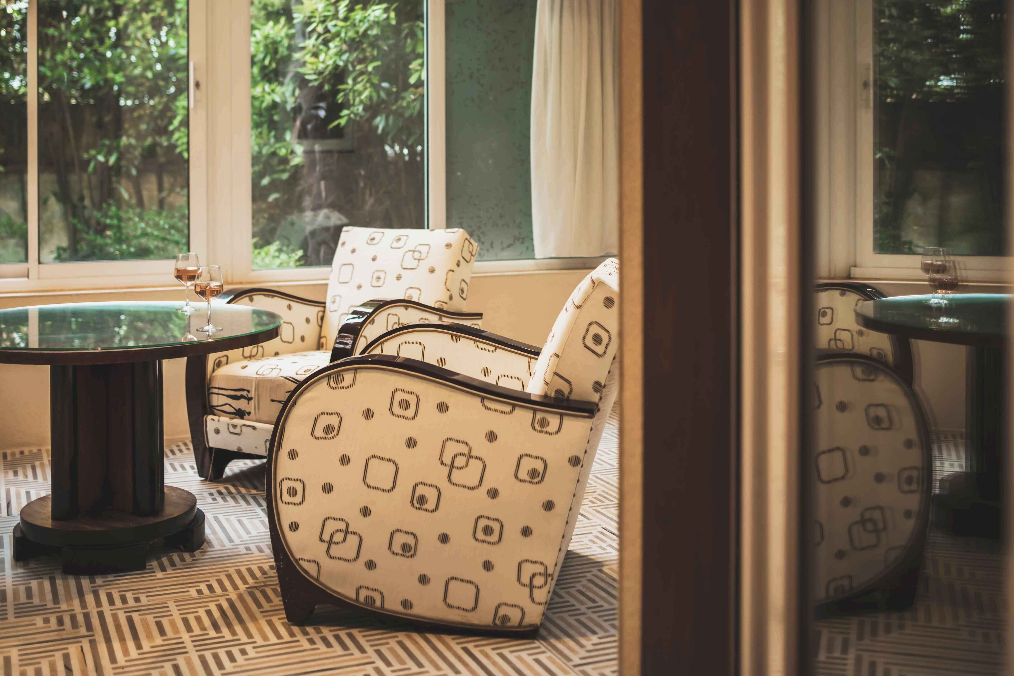 Quarto com poltronas estampadas, uma mesa de vidro redonda e vista para o verde lá fora.