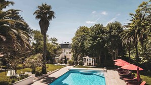 A swimming pool with lounge chairs and umbrellas, surrounded by palm trees and a building in the background. - Escapade Basque: jardin privé + près de la plage (Saint-Jean-de-Luz)