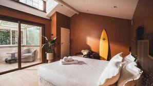 A bedroom with a large bed, a surfboard, and a sliding glass door leading to a balcony. - Escapade Basque: jardin privé + près de la plage (Saint-Jean-de-Luz)