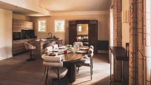 A spacious dining area with a round table, multiple chairs, and a kitchen in the background. - Jardin privé avec vue ville, proche plage (Saint-Jean-de-Luz)
