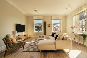 A living room with a sofa, armchair, TV, and windows with blinds. - Beautifully Designed Central Harrogate 2 Bed Apt (North Yorkshire)