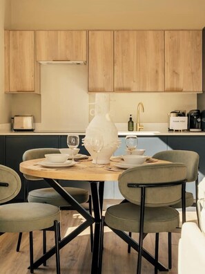 A modern kitchen with wooden cabinets, a round dining table, and four chairs. - Beautifully Designed Central Harrogate 2 Bed Apt (North Yorkshire)