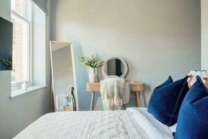 Een slaapkamer met een bed, een dressoir, een spiegel en een raam.