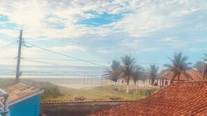 A coastal view with a beach, palm trees, and a building with a tiled roof. - Comfort and fun. Beachfront. Small pets are accepted. (Itanhaém)