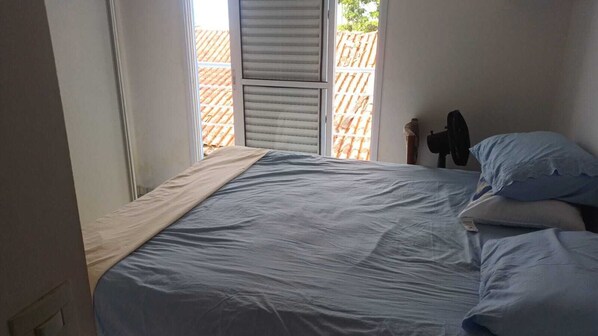 A bedroom with a bed, pillows, a window, and a view of a wooden fence.