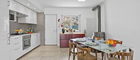 Una cocina moderna con armarios blancos, una mesa de comedor con sillas y vistas al exterior a través de una ventana.