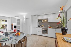 Una cocina moderna con armarios blancos, un comedor con mesa de vidrio y un jarrón con flores.