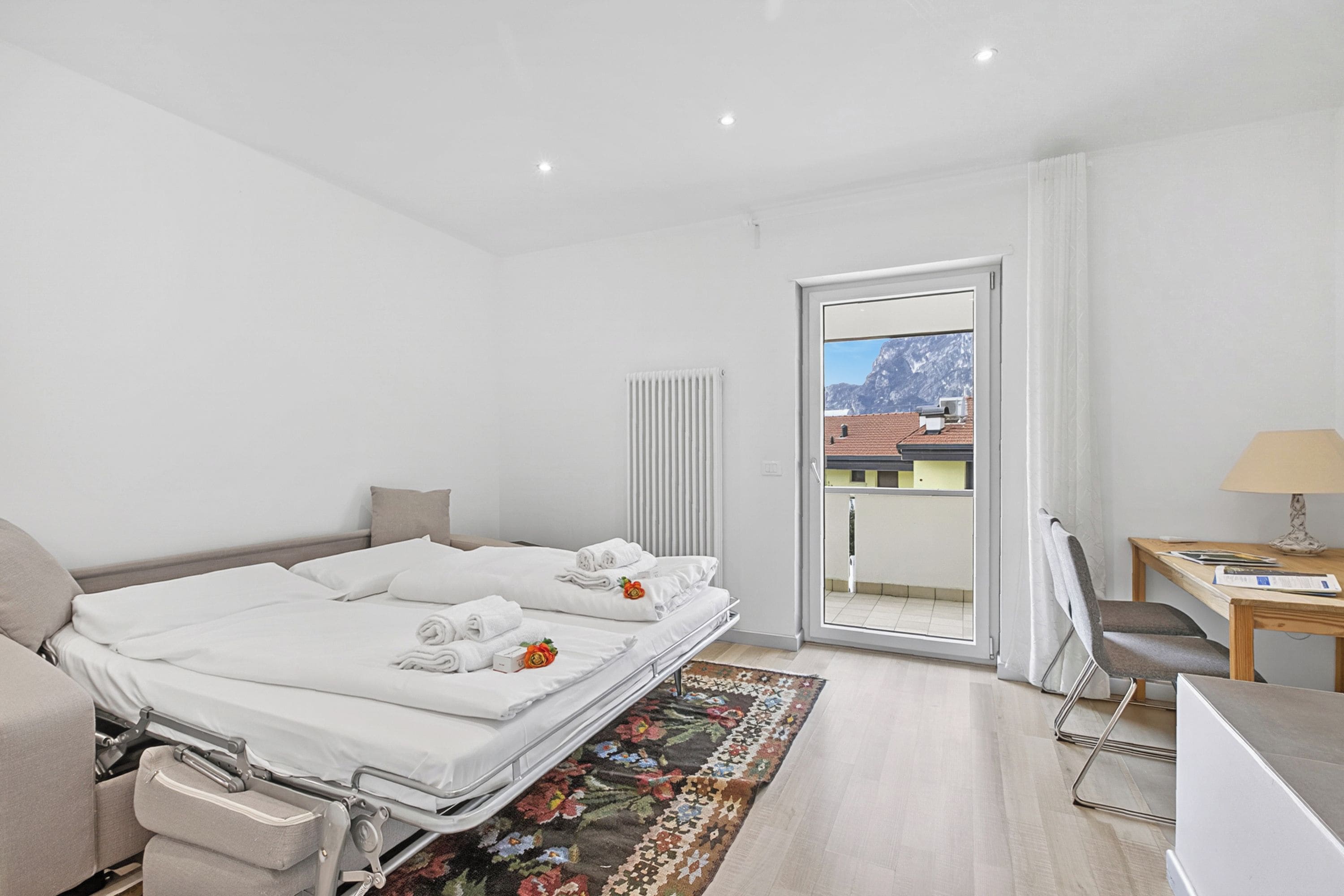 Habitación de hotel con cama, escritorio, silla, radiador y vistas al exterior.