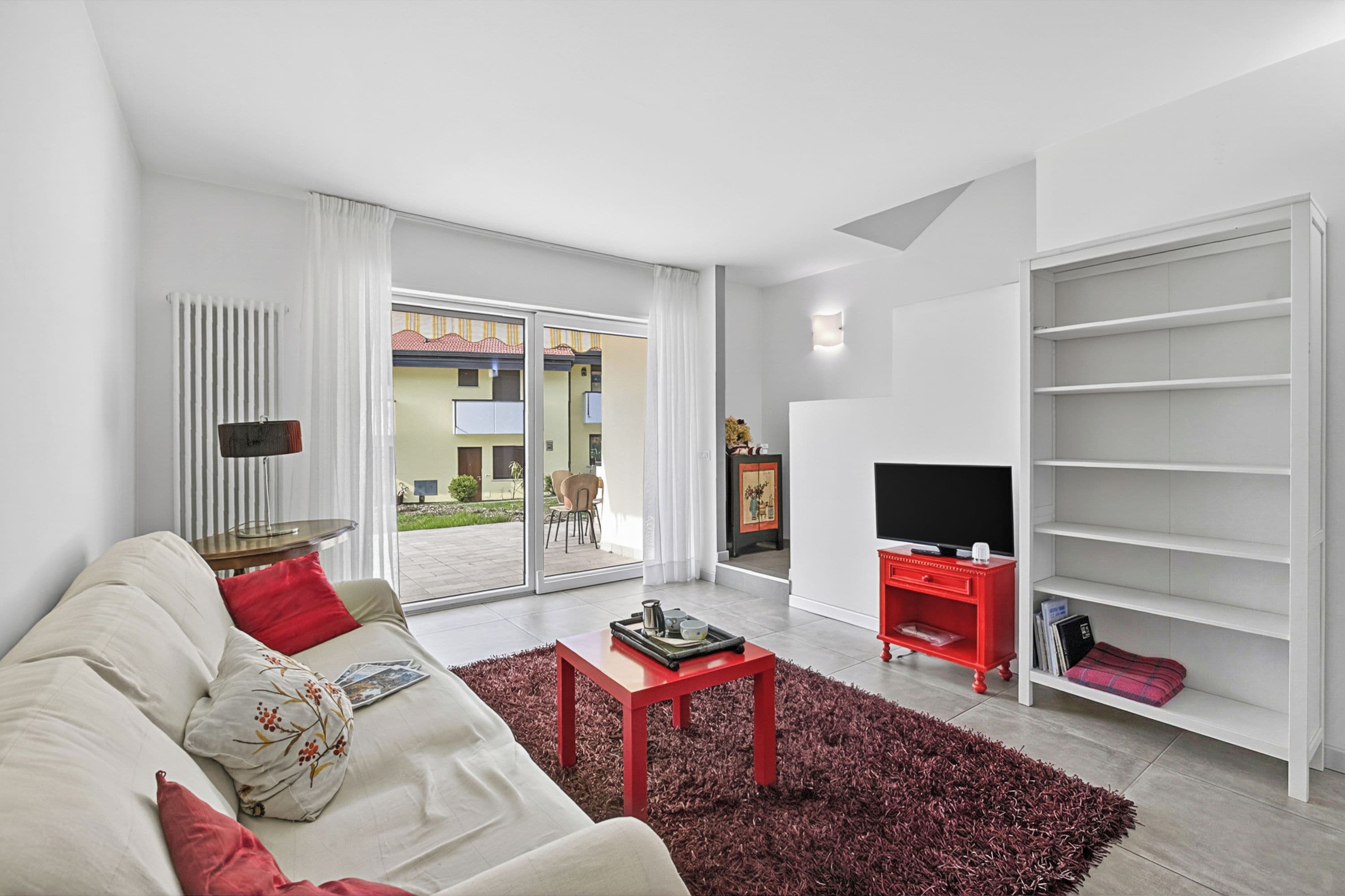 A modern living room with a sofa, a red coffee table, a TV stand, and a bookshelf.