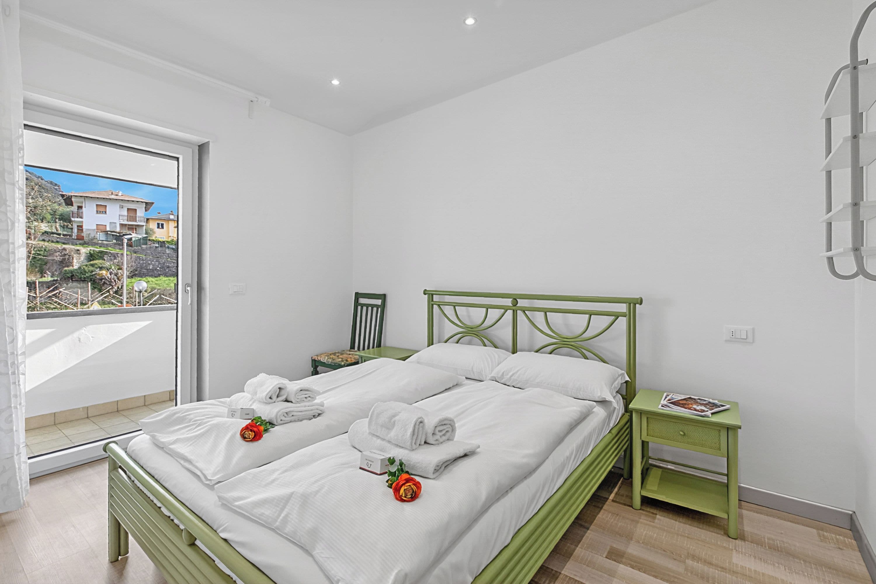 A bedroom with a bed, a nightstand, a window with a view, and a green metal headboard.