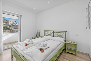 A bedroom with a bed, a nightstand, a window with a view, and a green metal headboard. - Olimpia Home - Terrace Dining and Pool (Tenno)