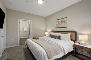 Une chambre à coucher avec un lit, des lampes de chevet, une carte accrochée au mur et une porte donnant sur une autre pièce.