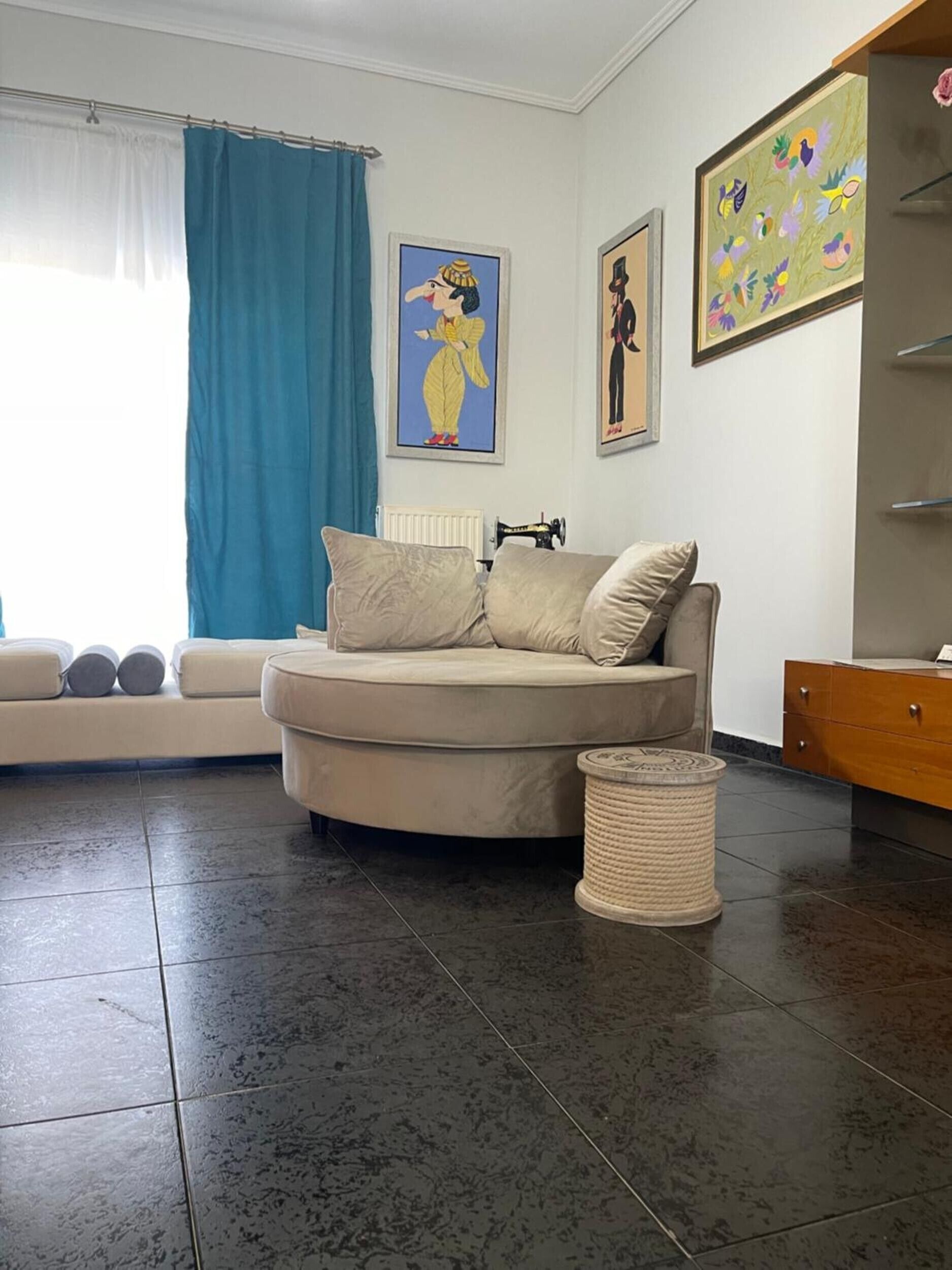 Un saló amb un sofà, una taula rodona petita, un radiador i una finestra amb cortines.