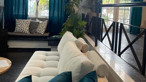 Una sala de estar con un sofá blanco, cortinas color esmeralda y vistas al exterior.