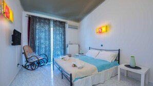 Un dormitorio con cama, una silla, una mesita de noche y un ventanal con cortinas.
